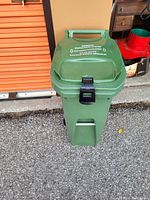 Front view of green compost bin closed, showing latch and warning on lid.