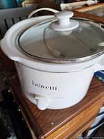White Bravetti electric cooking pot with glass lid on a wooden surface.