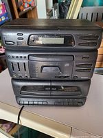 Stacked vintage electronic audio components: a Sansui CD player, a cassette deck, and an audio equalizer/amplifier on a white table.