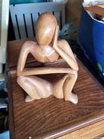Photo of hand-carved wooden figurine sitting in contemplative pose with head resting on hand