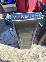 Front view of black tower heater showing vent grille and digital control panel with buttons and numeric display.