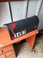 Side view of black metal mailbox showing red flag and exterior surface with some wear and scratches.