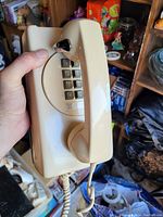 Photo of a beige rotary dial style telephone with push button dial and handset, showing front and one side, giving a clear view of dial and handset.