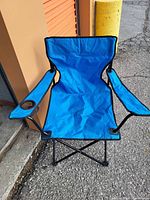 Photo showing assembled blue folding chair with cup holder on right armrest, folded metal frame visible beneath seat fabric.