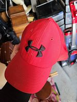 Red baseball cap with Under Armour black logo, front view showing structured crown and curved bill.
