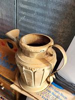 Photo of a vintage light beige ceramic watering can with detailed embossed design and curved handle, showing signs of age and use.