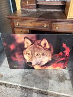 Rectangular print showing a close-up wolf's face with red leaves background placed on a wooden surface.