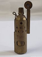Front view of vintage metal pocket lighter showing perforations and markings on body and hinged striker wheel arm