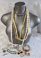 Costume jewelry displayed on bust including four beaded necklaces and various rings, earrings, brooches, and bracelets laid out below.