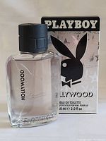 Photo of the iconic rectangular clear glass bottle with black cap displaying the Playboy Hollywood logo and text, with box in background.