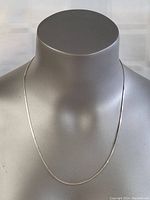 Silver necklace displayed on a mannequin bust showing full length and chain design.