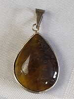 Clear image of teardrop-shaped brown stone pendant with silver-tone metal setting on white fabric background.