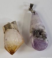 Photo showing both pendants: a rough citrine crystal pendant with metal wrap and a larger teardrop shaped purple amethyst pendant