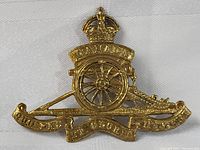Front view of the WW1 Canadian artillery cap badge showing the full design with crown, cannon, wheel, and inscriptions.