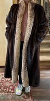 Model wearing full-length long fur coat, front view showing light brown fur trim.