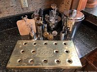 Brass bar drip tray with Kronenbourg 1664 logo and brass holes, surrounded by various bar utensils and ice bucket on black granite countertop.