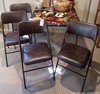 Four vintage brown faux leather folding chairs arranged in room with table behind