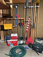 Full view of lot showing shovels, rakes, coolers, garden hose, flagpole, and other garden tools in a garage setting.