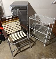 Full lot view showing Elfa wire mesh storage drawer unit, small white wire shelving unit with three wire shelves, and retro folding lawn chair with plastic slats and wooden armrests.