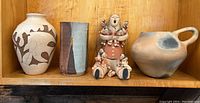 Four Native American pottery pieces on wooden shelf including storyteller figurine and three pottery vessels.