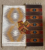 Large white and mustard yellow geometric wool rug with brown and orange woven table runner and four small woven coasters arranged on a carpeted floor.