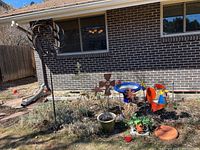 Overview of multiple lawn decorations including wind spinners, rooster sculpture, bird bath, clock, driftwood heart, and planter.