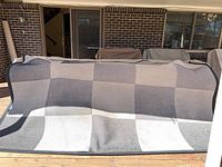 Outdoor patio rug draped over a bench showing its checkered gray pattern and visible use marks.