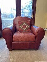 Front view showing full leather armchair with cushion in front of glass doors, highlighting shape and wear.