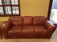 Front view of red three-seat leather sofa with rolled arms