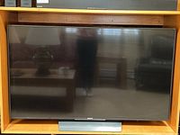 Front view of Sony 55 inch LCD TV in wooden cabinet showing screen and stand, reflection visible on screen.