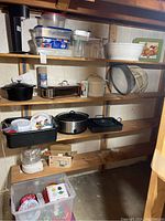 Full view of shelving with cast iron pot, slow cooker, plastic containers, strainer, and kitchen appliances.