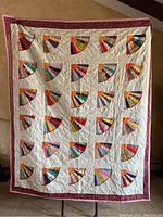 Full view of one handmade quilt with colorful fan-shaped patch blocks and maroon border.