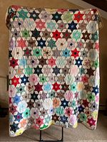 Full view of one quilt hung on stand showing multi-colored hexagon star pattern and scalloped edge