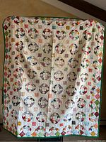 Full view of large handmade patchwork quilt showing repeated colorful circular ring patchwork blocks with diamond patchwork border and green outer edge.
