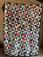 Full view of one of the handmade polyester quilts with colorful square patchwork and dark green border.