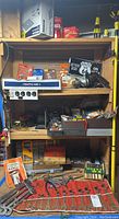 Full view of storage shelves with multiple boxes, tool sets, and loose hand tools including wrenches and drill bits visible