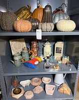 Photo of shelf with various decorative pumpkins on the top shelf, ceramic vanity items, stuffed Mickey Mouse doll, and vintage collectible bottles on the middle shelf, marble and stone trays and containers on the bottom shelf