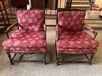 Front view of the two vintage armchairs with red floral upholstery and wooden frames showing wear.