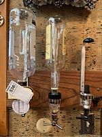 Wide view showing two inverted glass bottles mounted on a wooden board with dispensing mechanisms attached to the wall bar beverage dispenser.