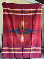 Full image of wool blanket showing overall geometric design with red base and multicolor stripes.