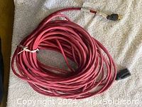 Photo showing a long red power cord coiled on a cloth surface with visible male and female plug ends.