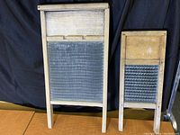 Two wooden washboards standing side by side, showing front view with metal scrubbing panels and wooden frames.