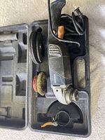 Rona electric angle grinder with multiple attachments including grinding disc and wire brush, stored in molded plastic tray inside case.