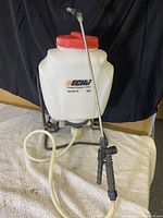 Front view of Echo branded white plastic tank backpack sprayer with red lid, attached hose and spray wand with trigger