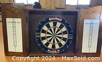 Front view with cabinet doors open showing Winmau Blade dartboard centered and dual white scoreboards.