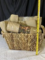 Front view of the woven basket filled with several rolled burlap fabric pieces, showing approximate height with measuring tape.
