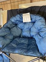 Large blue padded folding chair with deep cushioned seat and metal frame shown from front with instruction sheet on seat