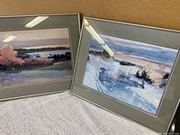 Two framed landscape paintings by Hayslette leaning against a wall, showing impressionistic natural scenes with water and trees in soft colors.