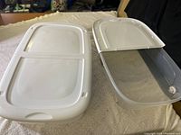 Photo showing two clear plastic rolling bins with white lids, one lid removed and placed next to bin.