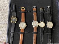Five corporate branded wristwatches with mixed leather straps displayed inside the black display attache.